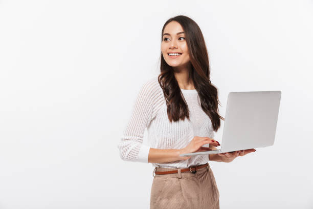 Portrait of a happy asian businesswoman holding laptop computer iand looking away solated over white background